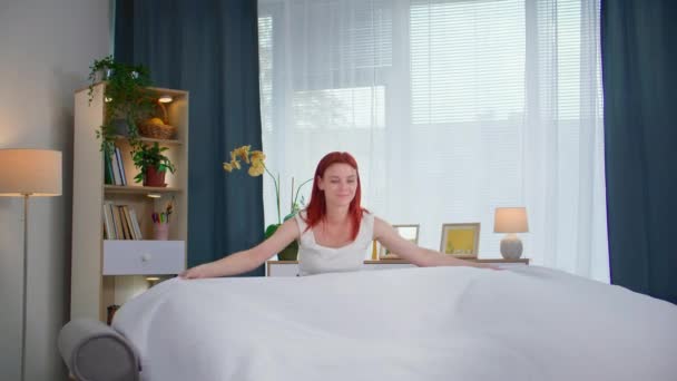muotokuva naispuolisesta kotiäidistä peittelemässä lakanaa nukkumisen jälkeen makuuhuoneessa kotona, hymyillen ja katsoen kameraa - Materiaali, video