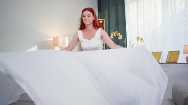 huiswerk, jonge vrouw het maken van bed met een wit laken terwijl schoonmaak kamer - Video