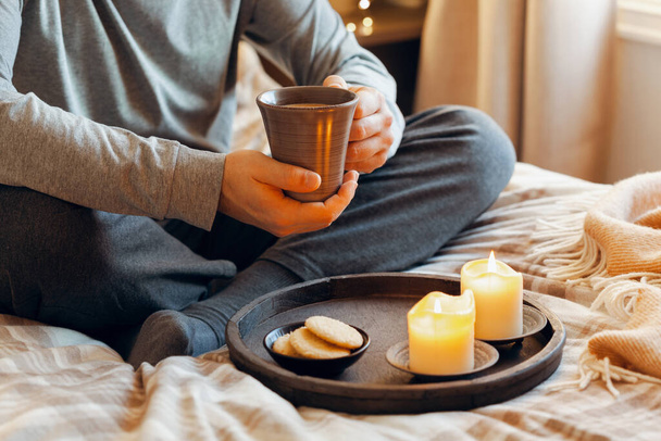 een blanke man die thuis ontspant, kaarsen aansteekt, koffie drinkt in bed - Foto, afbeelding