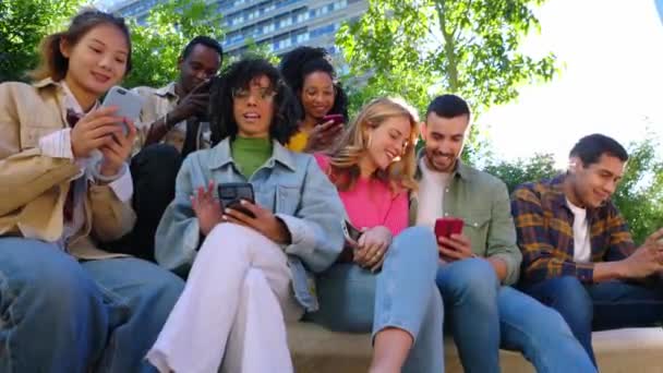 Junge Gruppe fröhlicher Menschen, die sich an der Stadtstraße mit dem Handy vergnügen. Lächelnde multiethnische Freunde, die draußen zusammen sitzen und sich Social-Media-Inhalte per Handy-App ansehen. Gen-Tech-Menschen-Konzept - Filmmaterial, Video