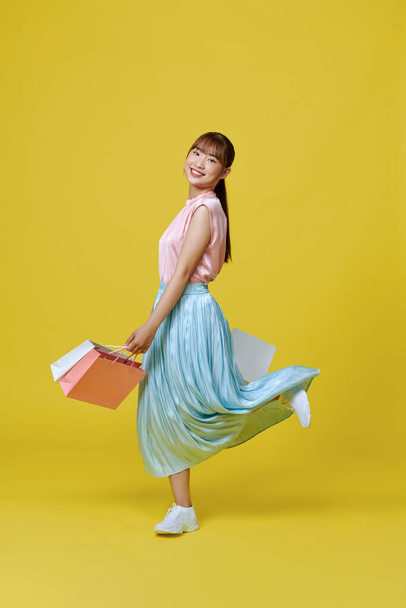 Full length profile of cute millennial lady  with bags isolated on yellow background - Photo, Image