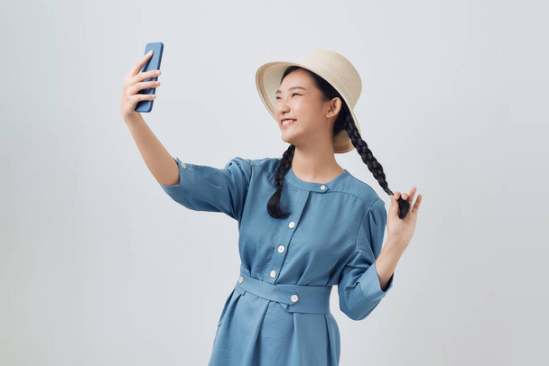 Azji dziewczyna pozowanie odizolowany na białym tle, robi selfie strzał na telefon komórkowy rozkładające ręce - Zdjęcie, obraz