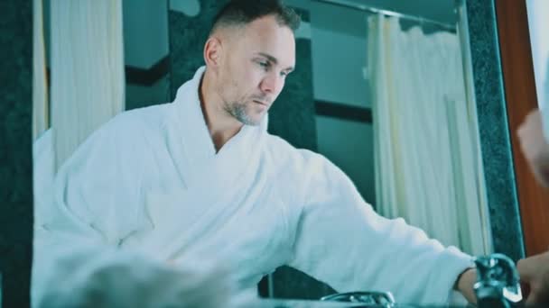 Mężczyzna kaukaski w jego 40-tych myje twarz przed lustrem w pokoju hotelowym i przygotowuje się do nocy - Materiał filmowy, wideo