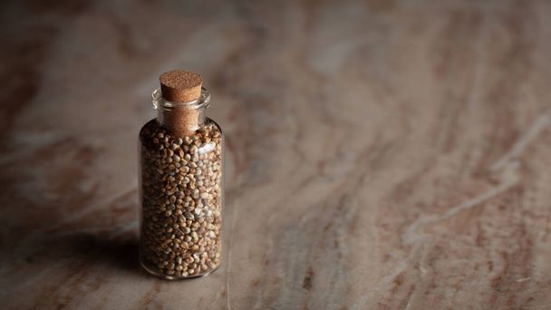 Una pequeña botella de vidrio llena de mijo perlado orgánico (Pennisetum glaucum) o Bajra se coloca sobre un fondo de mármol. - Foto, Imagen