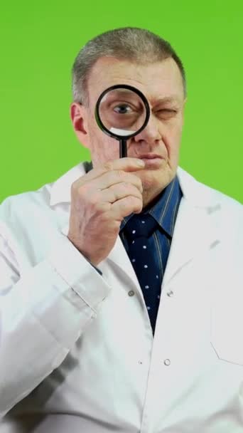 Senior doctor holding magnifying glass looking forward and have surprised face. Man looks at something and is very amazed by what he sees, looks with long face. Green screen, chroma key. Vertical. - Footage, Video