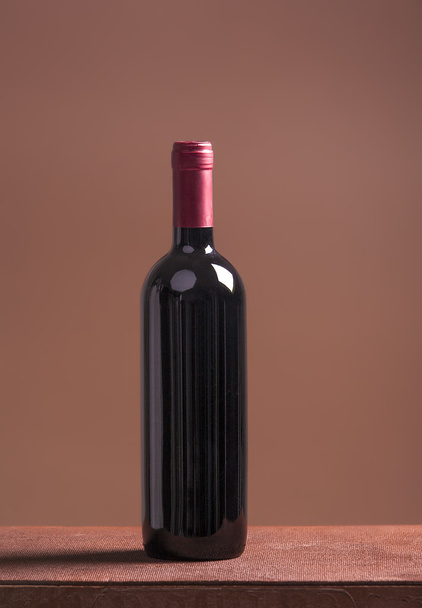 Red wine bottle on brown background - Фото, зображення