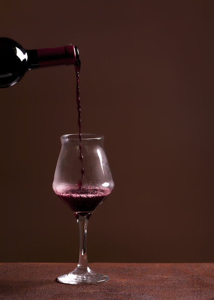 Rode wijn fles gieten wijnglas op bruine achtergrond - Foto, afbeelding
