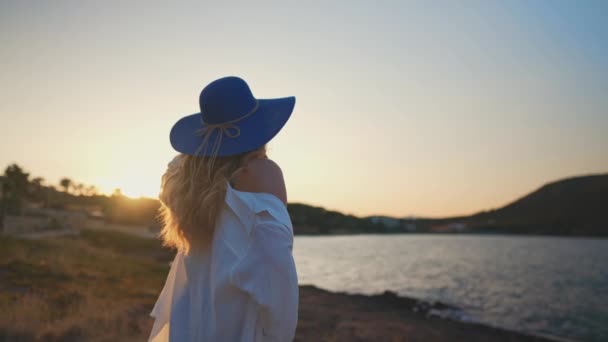Nainen sinisessä hatussa auringonlaskun aikaan meren rannalla.. - Materiaali, video