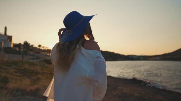Γυναίκα με μπλε καπέλο στο ηλιοβασίλεμα δίπλα στη θάλασσα. - Πλάνα, βίντεο