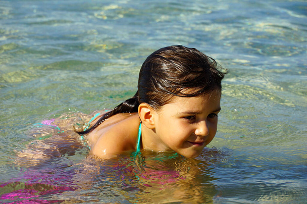 Söpö pikkutyttö leikkii ja kylpee kirkkaassa läpinäkyvässä merivedessä kesäpäivänä. - Valokuva, kuva