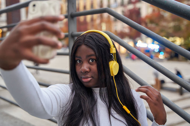 Afroamerikanerin mit gelben Kopfhörern macht ein Selfie mit einem Handy - Foto, Bild