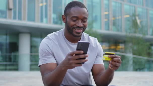 Africký Američan nakupování on-line držení smartphone placení zlatou kreditní kartou Guy na městské ulici ve městě nakupování na internetu zadat údaje o kreditní kartě on-line nakupování elektronického doručování - Záběry, video