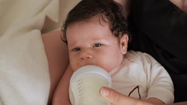 Mother gives little child to drink milk from plastic bottle. Infant lies in mother arms while consumes nutritious drink filled with vitamins - Footage, Video