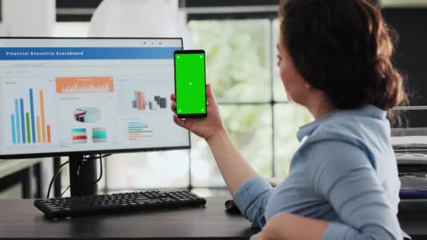 Employee holding mobile phone at desk, looking at isolated greenscreen layout presented on smartphone device. Businesswoman working with modern software technology, chromakey mockup. - Footage, Video
