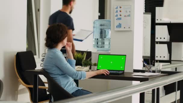 オフィスの従業員は,ノートパソコンのディスプレイにグリーンスクリーンを監視し,デスクで小規模な業務に取り組んでいます. モックアップコピースペースで隔離された染色体テンプレートを実行している画面を見ている人. - 映像、動画