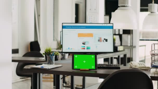Stůl s tabletem zobrazující zelenou obrazovku, prázdné pracoviště v kreativním agentuře kopracovním prostoru. Moderní gadget běží izolované chromakey displej v malém business pracovišti, makupy obrazovka. - Záběry, video