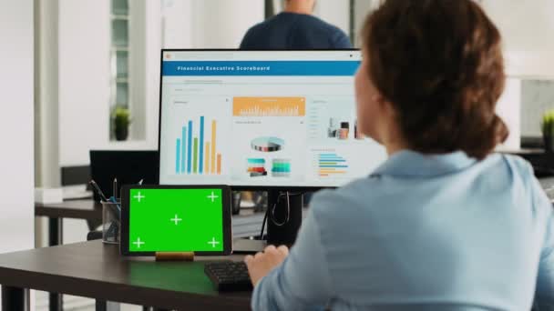 Офісний працівник перевіряє зелений екран на планшеті, працюючи над бізнес-операціями з ізольованим шаблоном копіювання та аналізуючи дані на комп'ютері за столом. Маючи гаджет з маком. - Кадри, відео