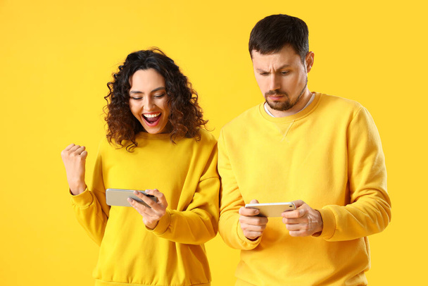 黄色の背景で携帯電話を使用している若いカップル - 写真・画像
