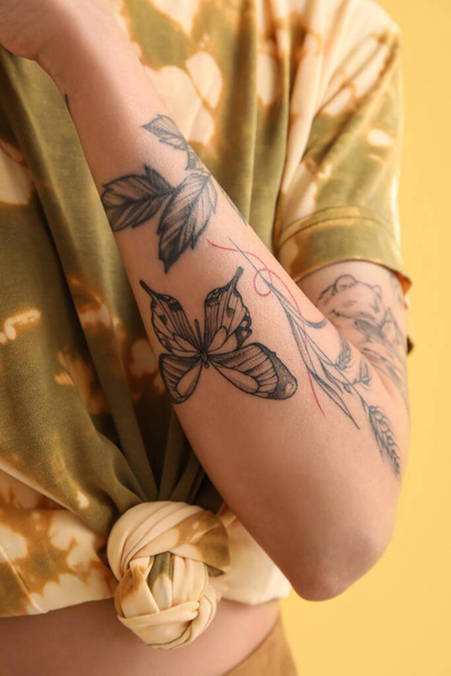 Young woman with tattooed arm on yellow background, closeup - Foto, Imagem