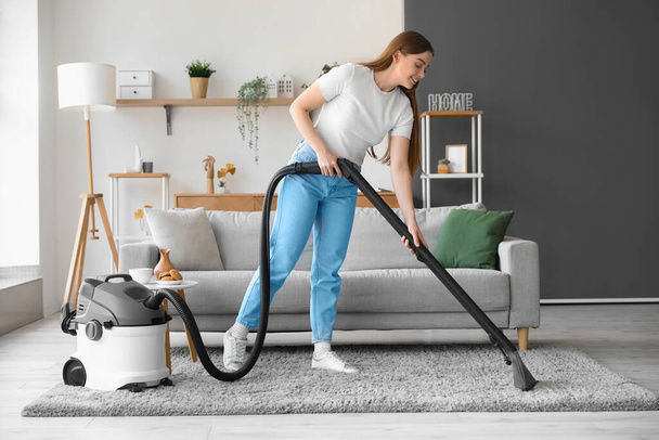 Young woman vacuuming carpet at home - Foto, immagini