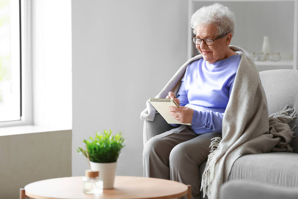 Idősebb nő otthon jegyzetfüzetbe ír. - Fotó, kép