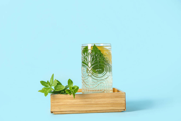 Деревянный мини-ящик со стаканом мятного чая и лимоном на синем фоне - Фото, изображение