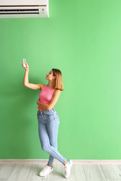 Nuori nainen kytkemällä ilmastointilaite lähellä vihreää seinää - Valokuva, kuva