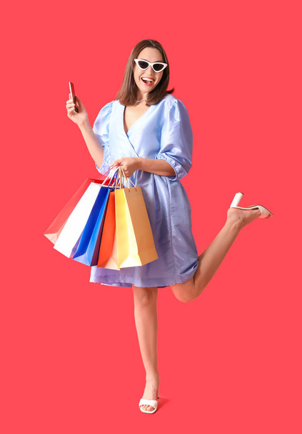 Nuori nainen ostoskassit ja matkapuhelin punaisella taustalla - Valokuva, kuva