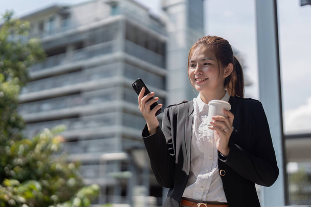 Jeune femme d'affaires asiatique professionnelle portant un costume à l'aide d'un téléphone mobile et parlant sur un téléphone mobile ayant un chat sur un téléphone portable marchant dans la rue de la ville urbaine. - Photo, image