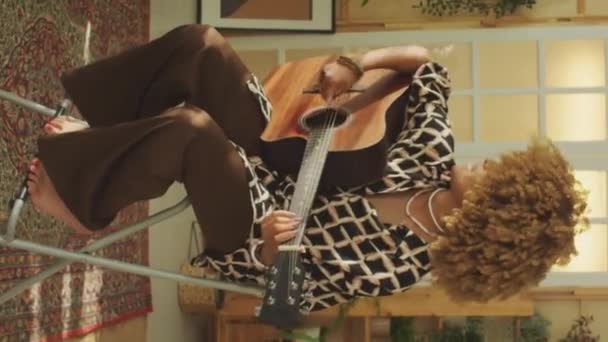Tiro vertical de un joven músico cantando una canción mientras toca la guitarra acústica en casa - Metraje, vídeo