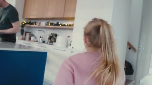 Valkoihoinen tyttö juoksee keittiöön, jossa vanhemmat kokkaavat ennen joulua. Laukaus punaisella heliumkameralla 8K.   - Materiaali, video