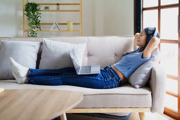 femme portant des écouteurs sur un canapé confortable en écoutant utiliser un ordinateur portable et de la musique - Photo, image