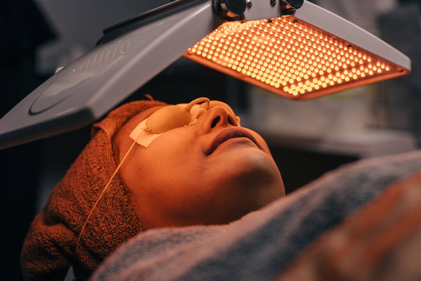 バイオライトLEDレーザーを使用した女性の顔の化粧品プロセス 技術の美容スパで若返りを持ち上げる皮膚治療修理 - 写真・画像