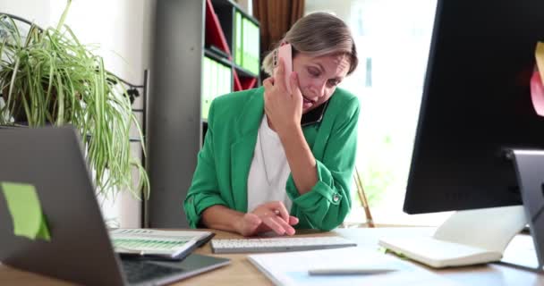 Απασχολημένος διευθυντής συμβουλεύεται τον πελάτη στο τηλέφωνο, διαχειρίζεται στατιστικά δεδομένα στο laptop. Επιχειρηματική γυναίκα ασχολείται με την πολλαπλή απασχόληση στο χώρο εργασίας στο γραφείο στο σπίτι - Πλάνα, βίντεο