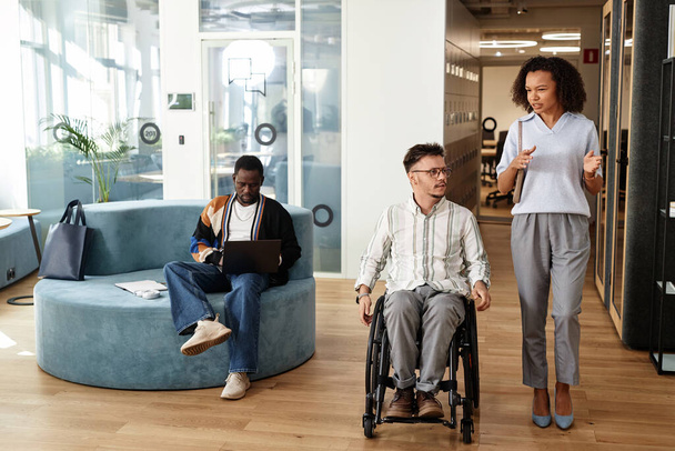 Mladá podnikatelka mluví se svým kolegou se zdravotním postižením, zatímco oni procházejí chodbou v kanceláři - Fotografie, Obrázek