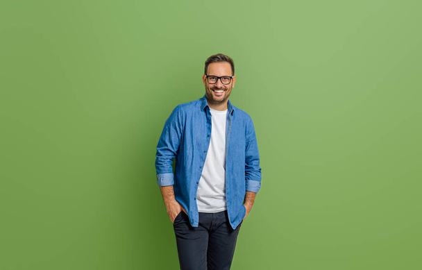 Nuoren liikemiehen muotokuva kädet taskussa seisoo eristettynä vihreää taustaa vasten - Valokuva, kuva