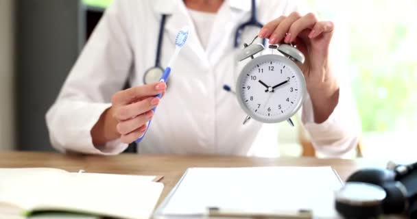 Doctor dentist holds toothbrush and alarm clock. Time for proper dental hygiene - Footage, Video