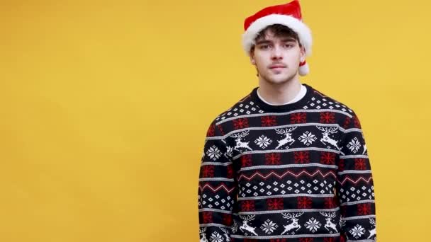 Kaukasischer junger Mann mit Weihnachtsmann-Hut, der isoliert auf den Hintergrund zeigt - Filmmaterial, Video