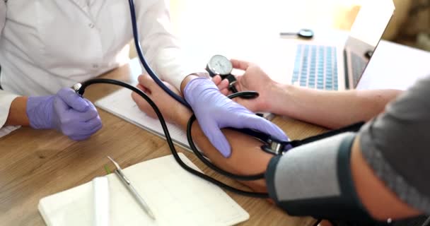 Médico cardiólogo terapeuta mide la presión arterial del hombre paciente en la clínica. Control de la presión arterial y enfermedades cardiovasculares - Imágenes, Vídeo