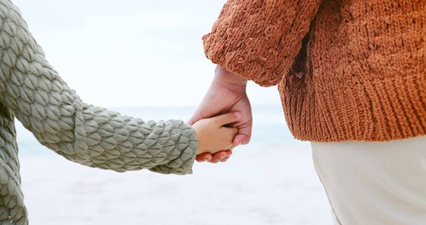 Rodzic, dziecko i trzymanie się za ręce nad oceanem dla miłości, opieki lub wsparcia w zaufaniu, podróży lub ucieczki na świeżym powietrzu. Zbliżenie osoby z dzieckiem dla jedności, więzi lub współczucia na plaży lub wybrzeżu morskim razem. - Zdjęcie, obraz