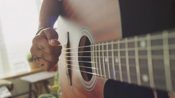 Крупним планом руки невпізнаваної жінки, використовуючи пік під час гри на акустичній гітарі в приміщенні - Кадри, відео