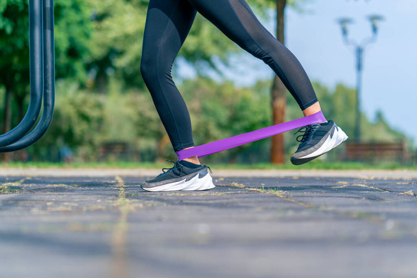 Ноги девушки спортивного тренера, выполняющего упражнения с эластичной лентой для укрепления мышц на спортивной площадке - Фото, изображение