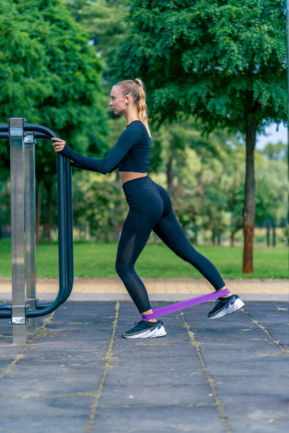 Atleta ragazza concentrata esegue esercizi con un elastico sportivo su macchine da ginnastica stradale - Foto, immagini
