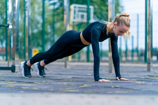 Спортивная девушка выполняет упражнения доски для укрепления всех мышечных групп тела во время утренней тренировки на спортивной площадке - Фото, изображение