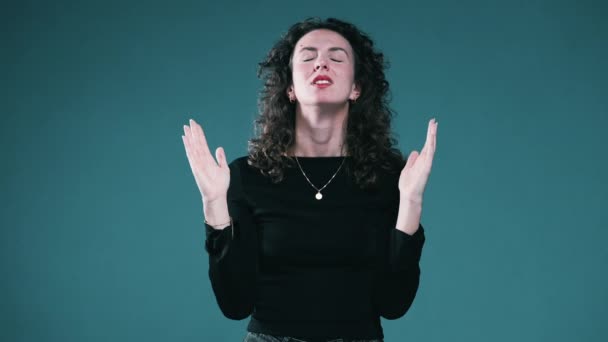 Spirituelle Frau im Gebet mit offenen Armen, die mit Hoffnung und Gratulation aufblickt, während sie auf blauem Hintergrund steht - Filmmaterial, Video