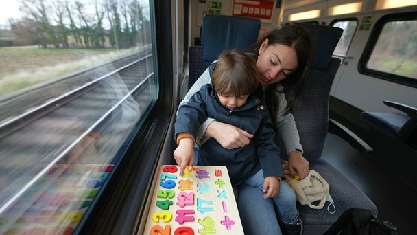 Poświęcona matka i jej dziecko uczestniczą w zadaniu związanym ze szkołą na pokładzie pociągu dużych prędkości, produktywnie wykorzystując czas podróży - Zdjęcie, obraz
