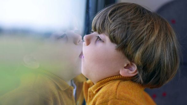 Bored funny small boy with face glued on trian window. Mouth and lips pressed on glass and staring at landscape scenery pass by in transportation - Photo, Image