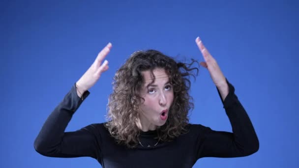 Lustige Frau imitiert Kopfexplosion auf blauem Hintergrund, schockiert und doch amüsiert, eine bahnbrechende Idee zu haben, sich aufgeklärt zu fühlen - Filmmaterial, Video
