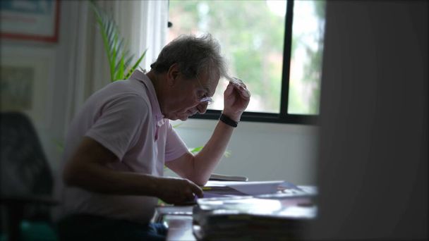 Een openhartige senior die thuis documenten inspecteert, concentreerde zich op het lezen van papierwerk. Oudere persoon op kantoor - Foto, afbeelding