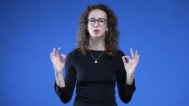 Frau in Meditationspose mit den Händen, während sie mit geschlossenen Augen auf blauem Hintergrund steht und einen tiefen Atemzug nimmt, um Stress abzubauen - Filmmaterial, Video